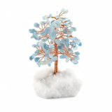 Copper tree with aquamarine gemstone leaves rooted in a raw white crystal base against a white background for spiritual home decor.