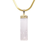 Close-up of raw rectangular selenite stone pendant in gold-tone setting on white background.