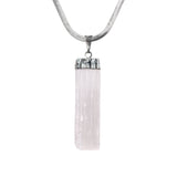 Close-up of raw rectangular selenite stone pendant in silver-tone setting on white background.