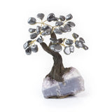 Small hematite bonsai tree with polished gemstone leaves on raw amethyst crystal base.